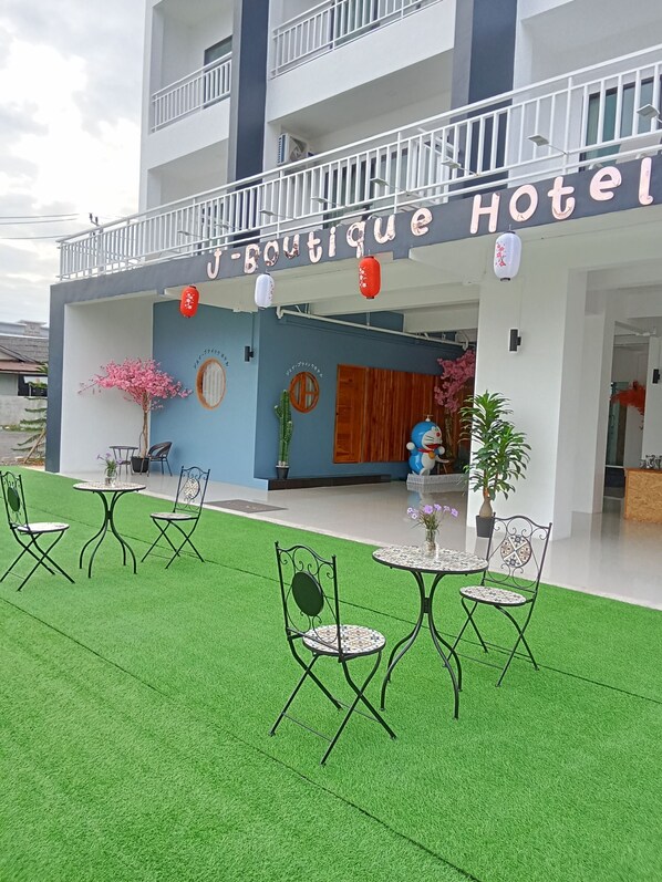 Un hotel boutique con diseño moderno, que cuenta con un balcón con barandillas blancas, un cartel con el nombre del hotel y una zona de estar con mesas y sillas.