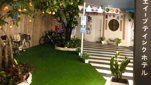 A building with a white exterior, a small garden with green grass, and a bicycle parked outside. - J-Boutique Hotel (Khon Kaen)