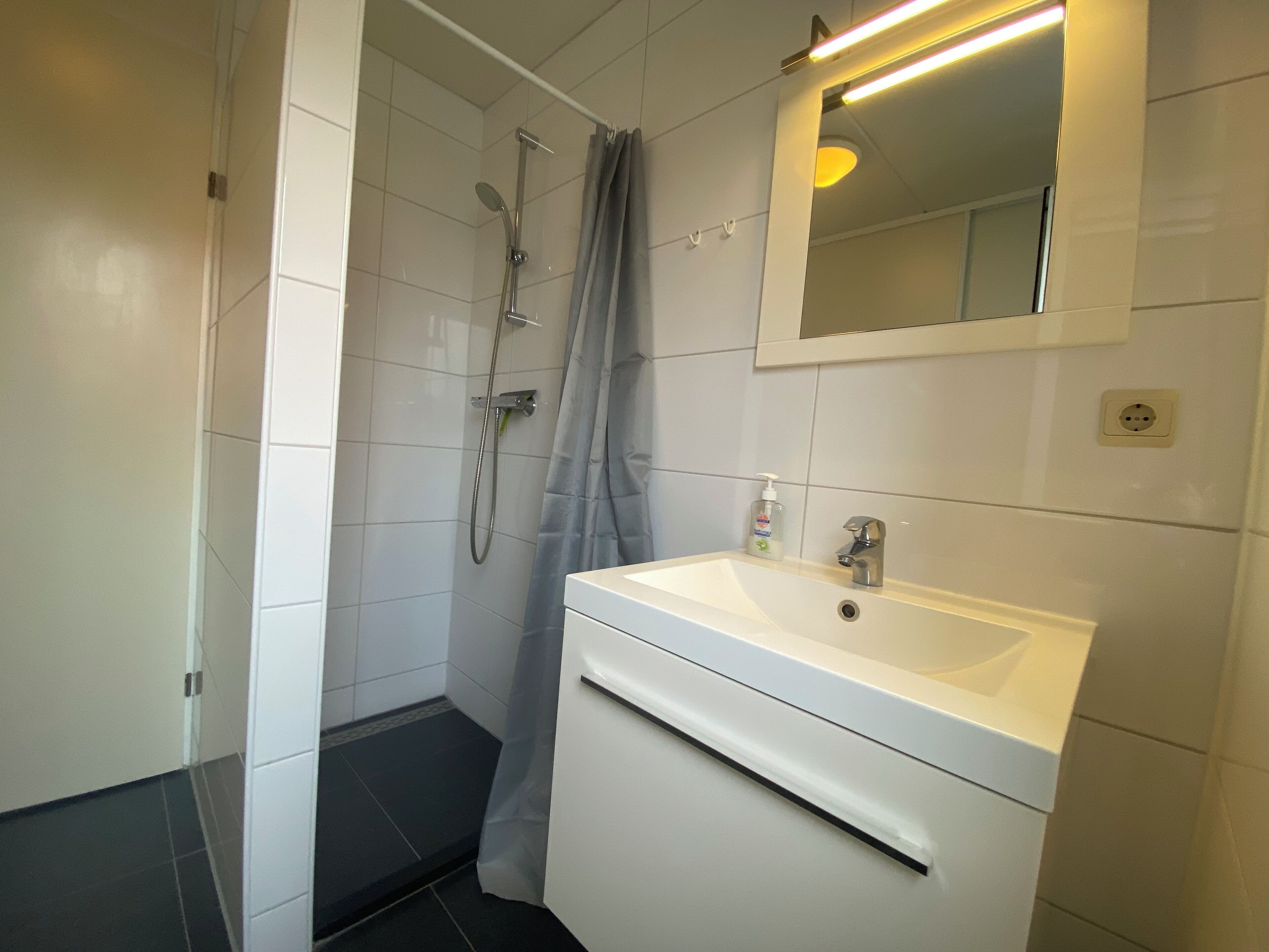 Een badkamer met een wit wastafel, spiegel en douche.