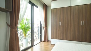 A bedroom with a large wardrobe, a bed, and a sliding glass door leading to a balcony with a potted plant.
