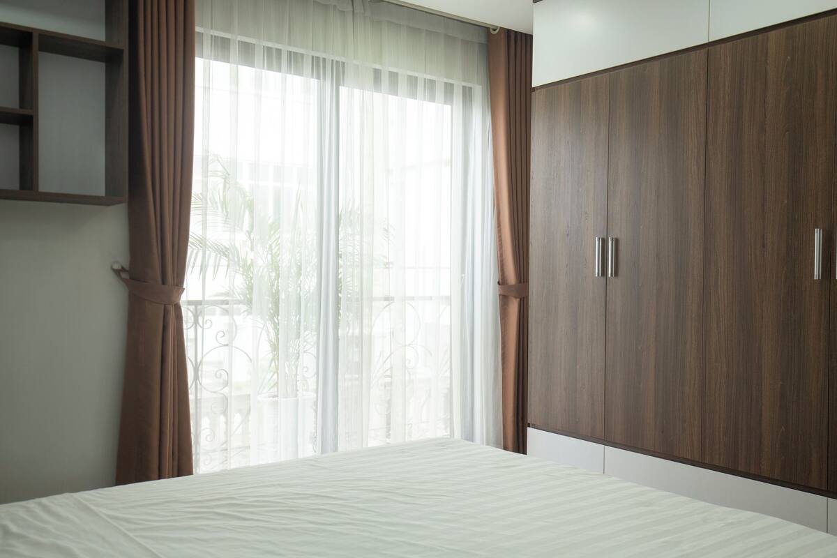 Ein Schlafzimmer mit einem großen Bett, einem Holzschrank und transparenten Vorhängen.