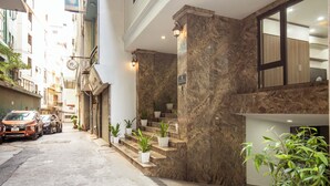 A hotel entrance with a marble staircase, potted plants, and a view of the street.