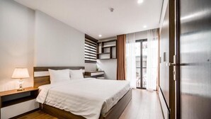 A modern hotel room with a wooden bed, a bedside table with a lamp, a built-in wardrobe, and a view of the outside.