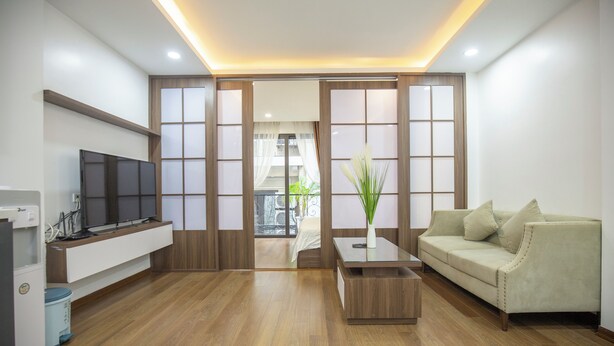 A modern living room with a flat-screen TV, a sofa, a coffee table, and a sliding door leading to a balcony.