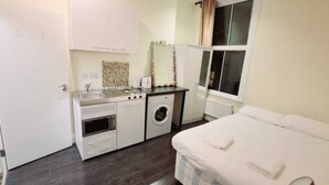 Een compacte hotelkamer met een bed, een kleine kitchenette met een magnetron, een wasmachine en een spoelbak.