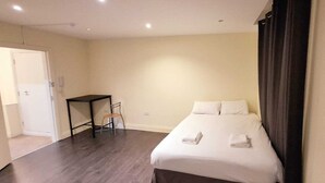 Een hotelkamer met een bed, een stoel, een klein tafeltje en een deur.