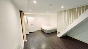Een moderne, goed verlichte hal met een trap die naar een slaapkamer leidt. De kamer heeft een bed, een garderobe en een witte deur.