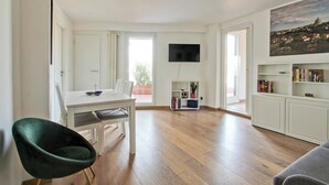 Amplia sala de estar con una mesa de comedor, una silla verde, una estantería y un televisor de pantalla plana montado en la pared.
