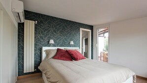 Un dormitorio con cama, radiador, puerta y vistas al exterior.