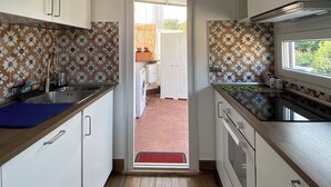 Una cocina estrecha con armarios blancos, encimera azul y salpicadero con diseño. Se ve un tapete rojo en la entrada.