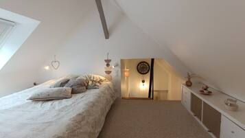 A bedroom with a sloped ceiling, a bed with patterned bedding, a bedside table with decorative items, and a wall-mounted light fixture.