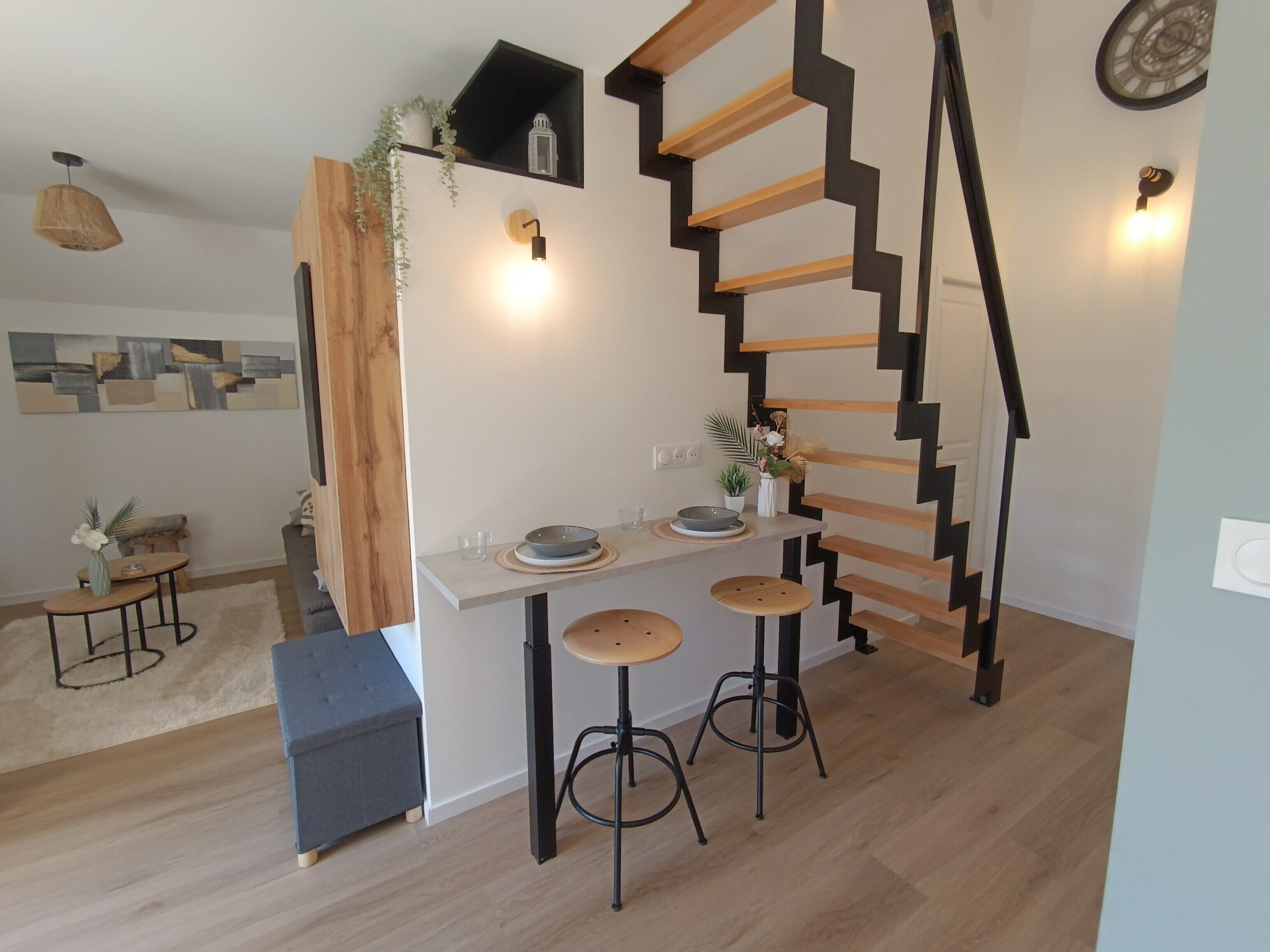A modern kitchen with a wooden staircase, a dining area with stools, and a small seating area with a bench.