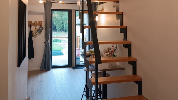 Ein modernes Interieur mit einer Holztreppe, einer Deckenleuchte und Blick durch eine Glastür.