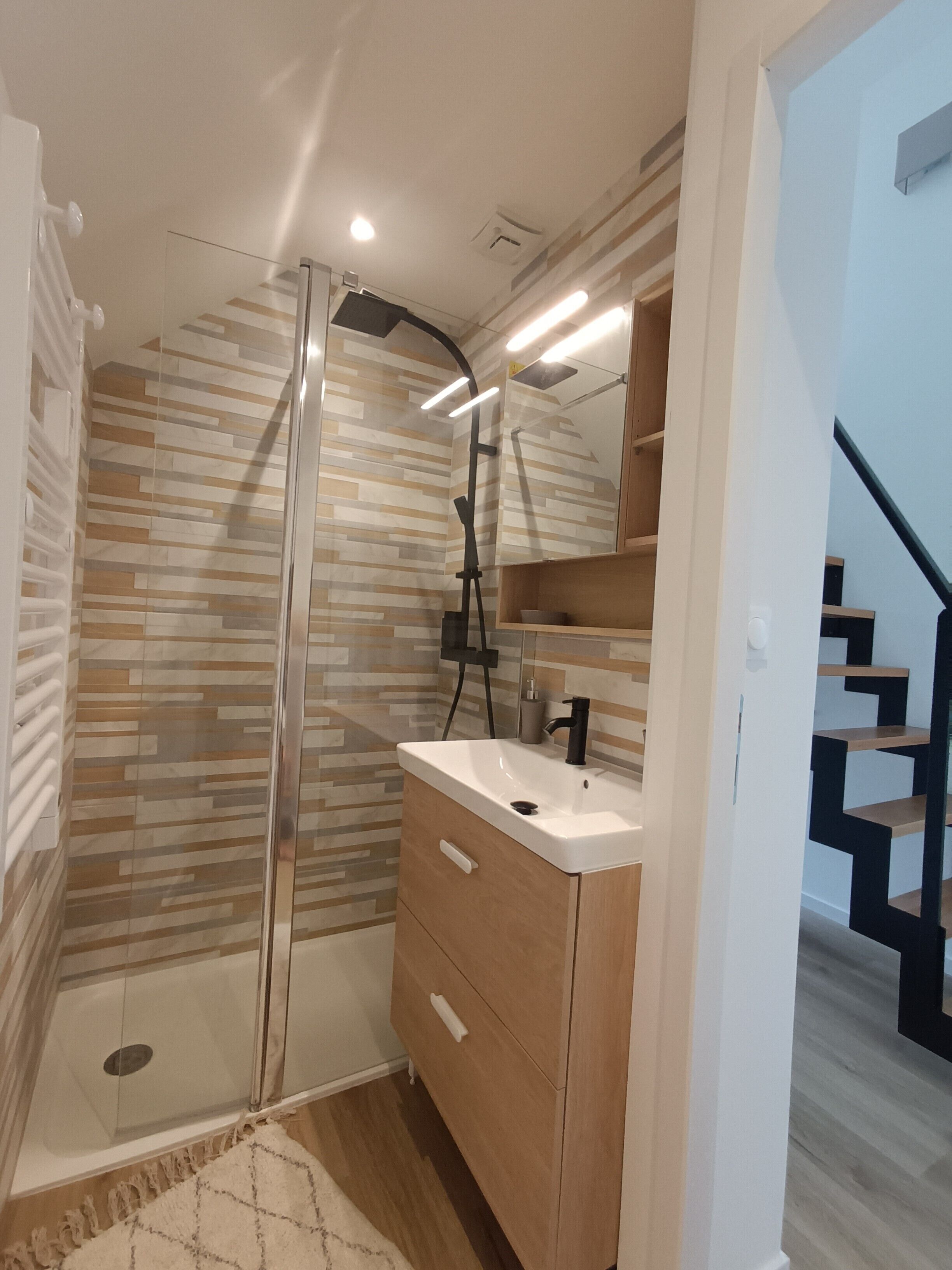 Een moderne badkamer met een douchecabine van glas, een houten wastafelmeubel met een wastafel en een spiegel erboven.