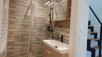 Een moderne badkamer met een douchecabine van glas, een houten wastafelmeubel met een wastafel en een spiegel erboven.