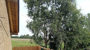 Eine Holzterrasse mit Tisch und Stühlen, ein kleiner Tisch mit Dekoration und Blick auf eine grüne Landschaft mit Bäumen.