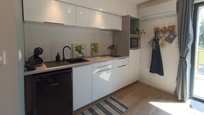Eine moderne Küche mit weißen Schränken, einem schwarzen Geschirrspüler, einem eingebauten Ofen und einem kleinen Fenster mit Vorhängen.