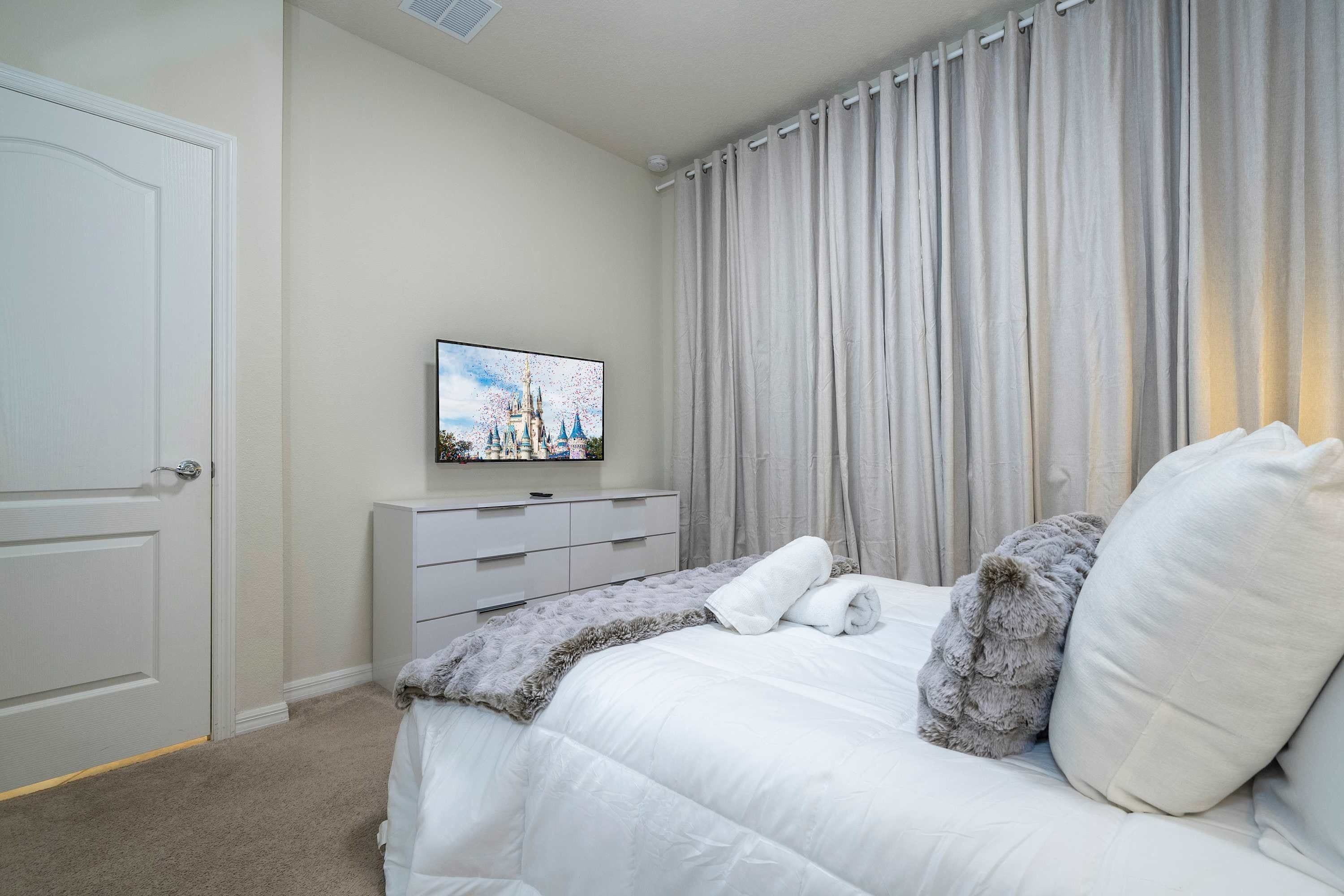 A bedroom with a bed, a television on a dresser, and a window with curtains.