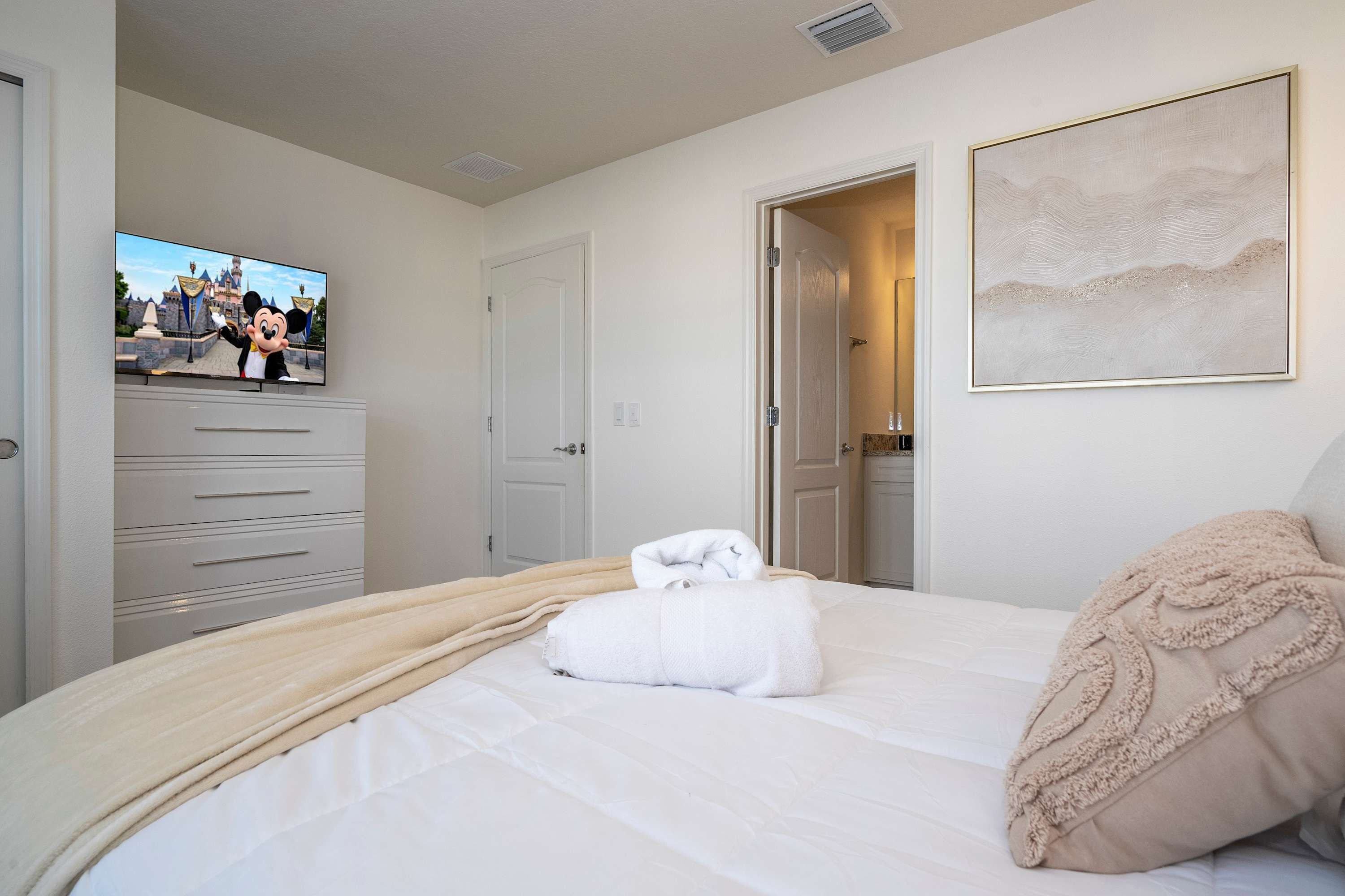 Habitación de hotel con cama, televisor mostrando un personaje de dibujos animados, puerta y un cuadro en la pared.