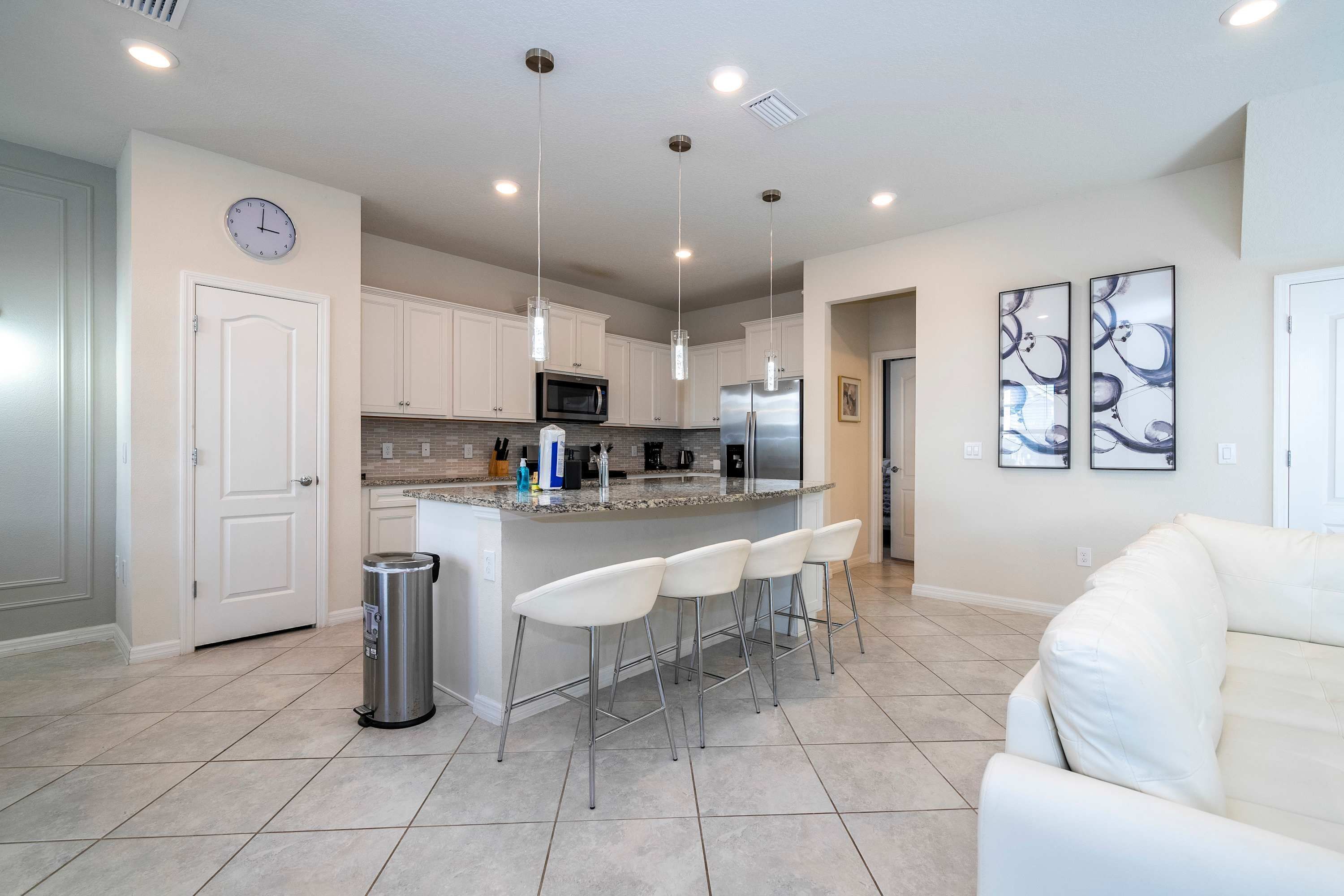 A modern kitchen with white cabinets, stainless steel appliances, and a central island with bar stools.