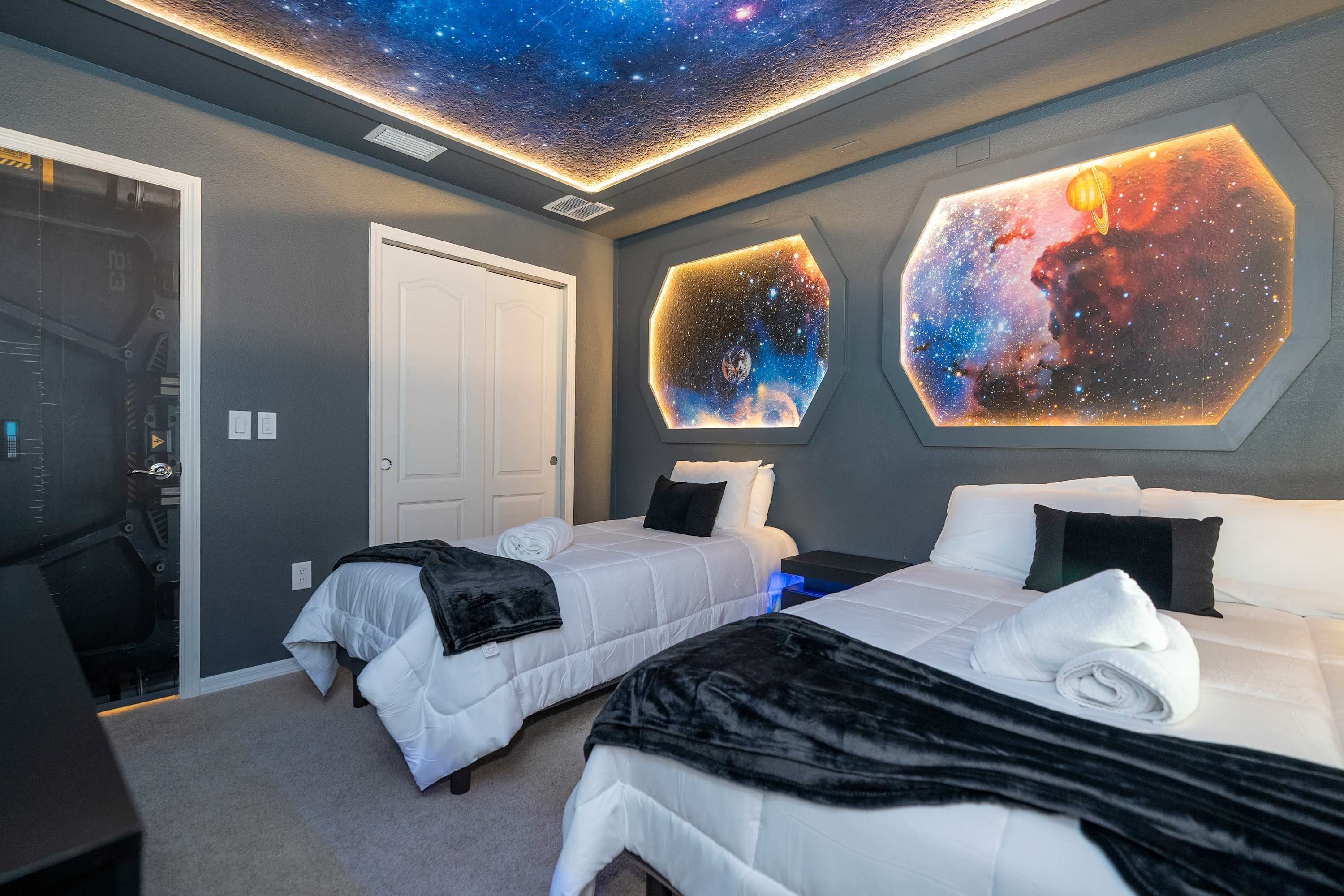 A bedroom with two beds, a desk, and a ceiling with a starry night design.