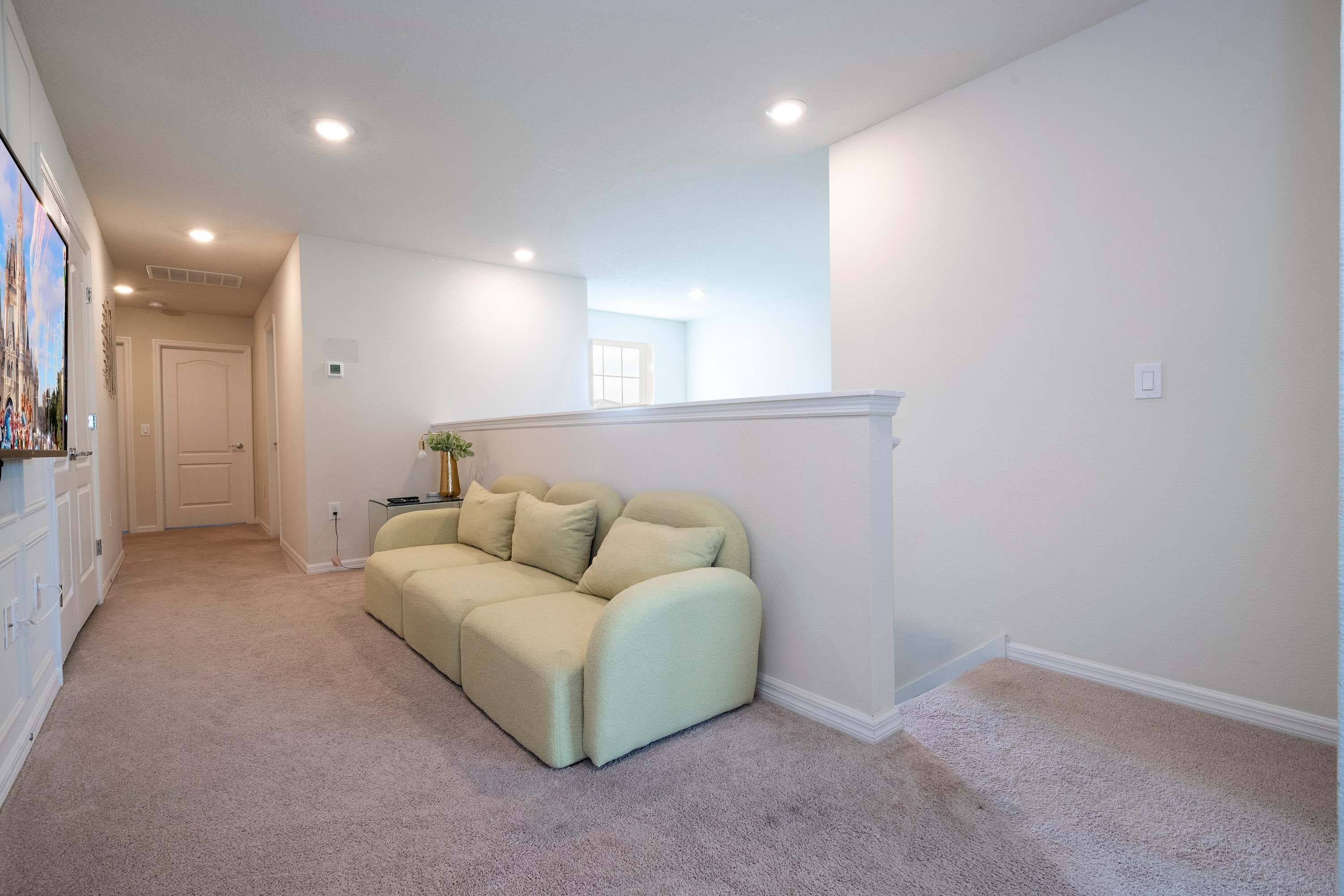 A hallway with a beige sofa, white walls, and a door at the end.