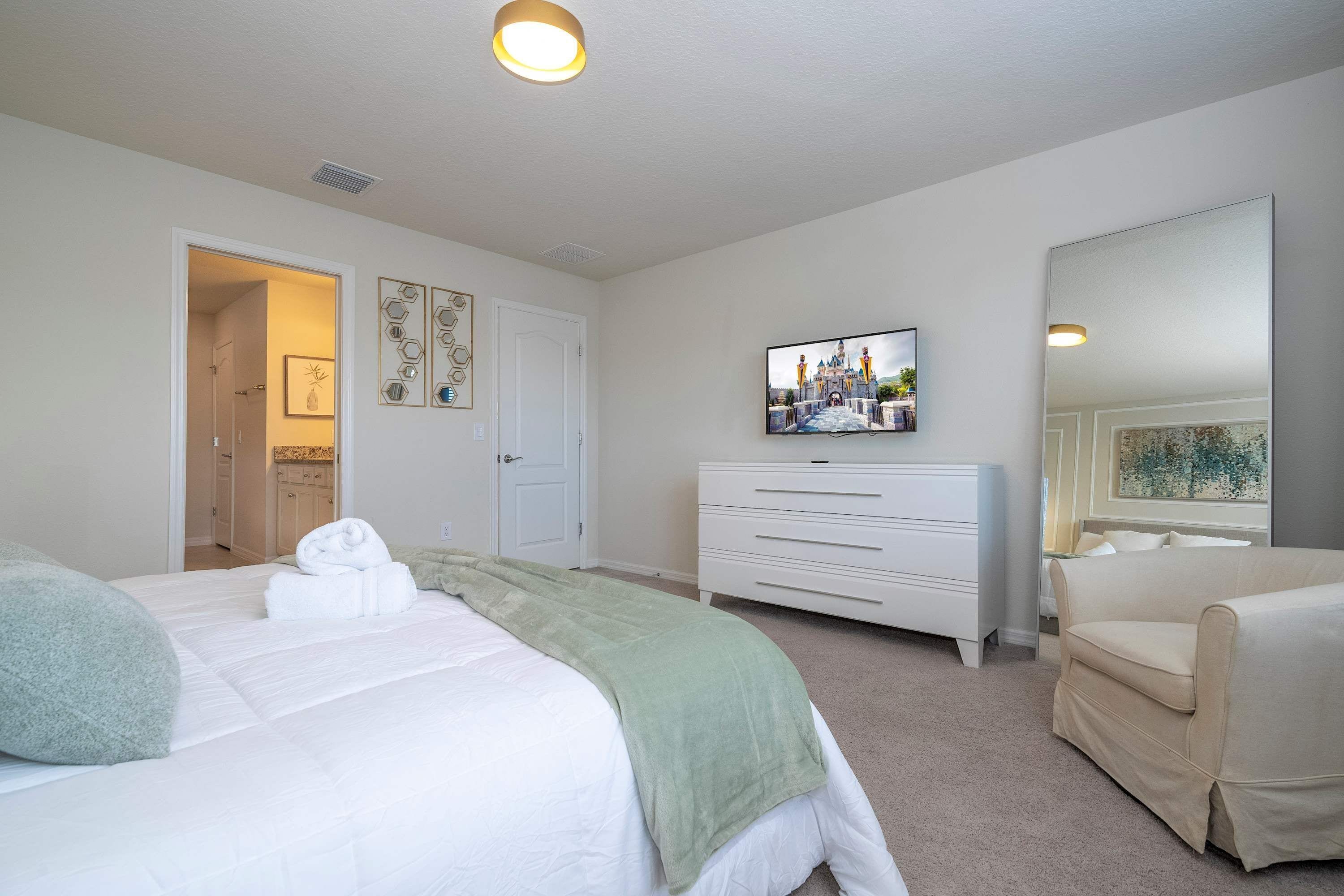 A bedroom with a bed, a dresser, a TV, and a mirror.