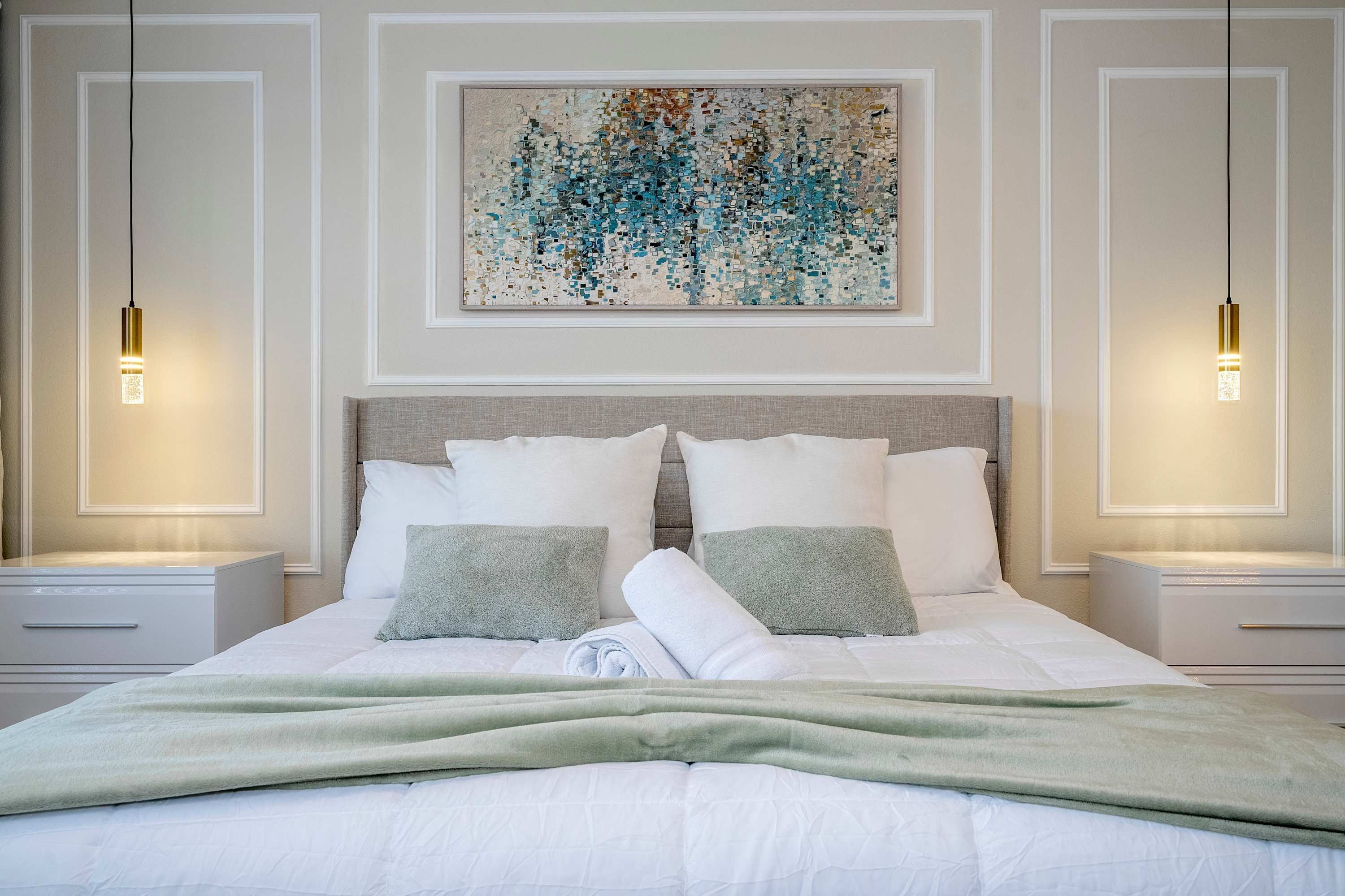 A neatly made bed with white bedding and a green throw blanket, flanked by two bedside tables with lamps.