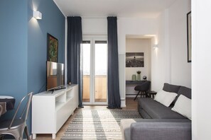 Uma sala de estar moderna com um sofá cinza, um móvel de entretenimento branco e uma janela grande com cortinas.