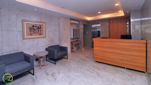 A modern lobby with marble flooring, a reception desk, a seating area with sofas and a small table, and a framed artwork on the wall. - MZapartments Ataulfo Leblon (Rio de Janeiro)