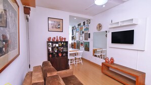 A living room with a brown sofa, a wooden coffee table, a TV mounted on the wall, and a white dining area with chairs. - MZapartments Ataulfo Leblon (Rio de Janeiro)
