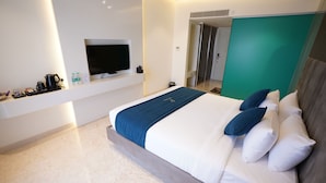 Une chambre d’hôtel moderne dotée d’un grand lit, d’une télévision à écran plat, d’une machine à café et d’une armoire de couleur turquoise.
