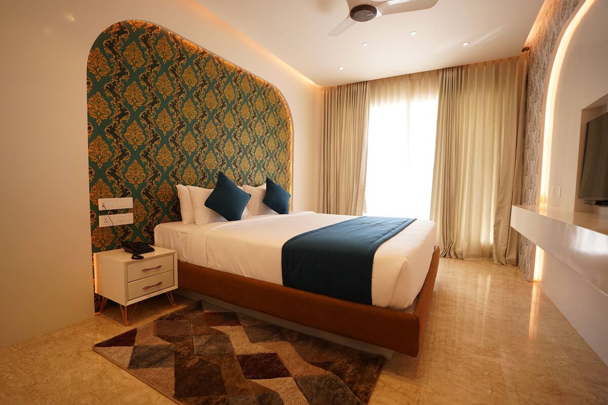 Una habitación de hotel moderna con una cama grande, una mesita de noche, un televisor y un cabecero estampado.