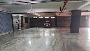 Un vaste parking, doté d’un sol poli, où une voiture rouge est garée au centre, et où une personne se tient près de l’entrée.