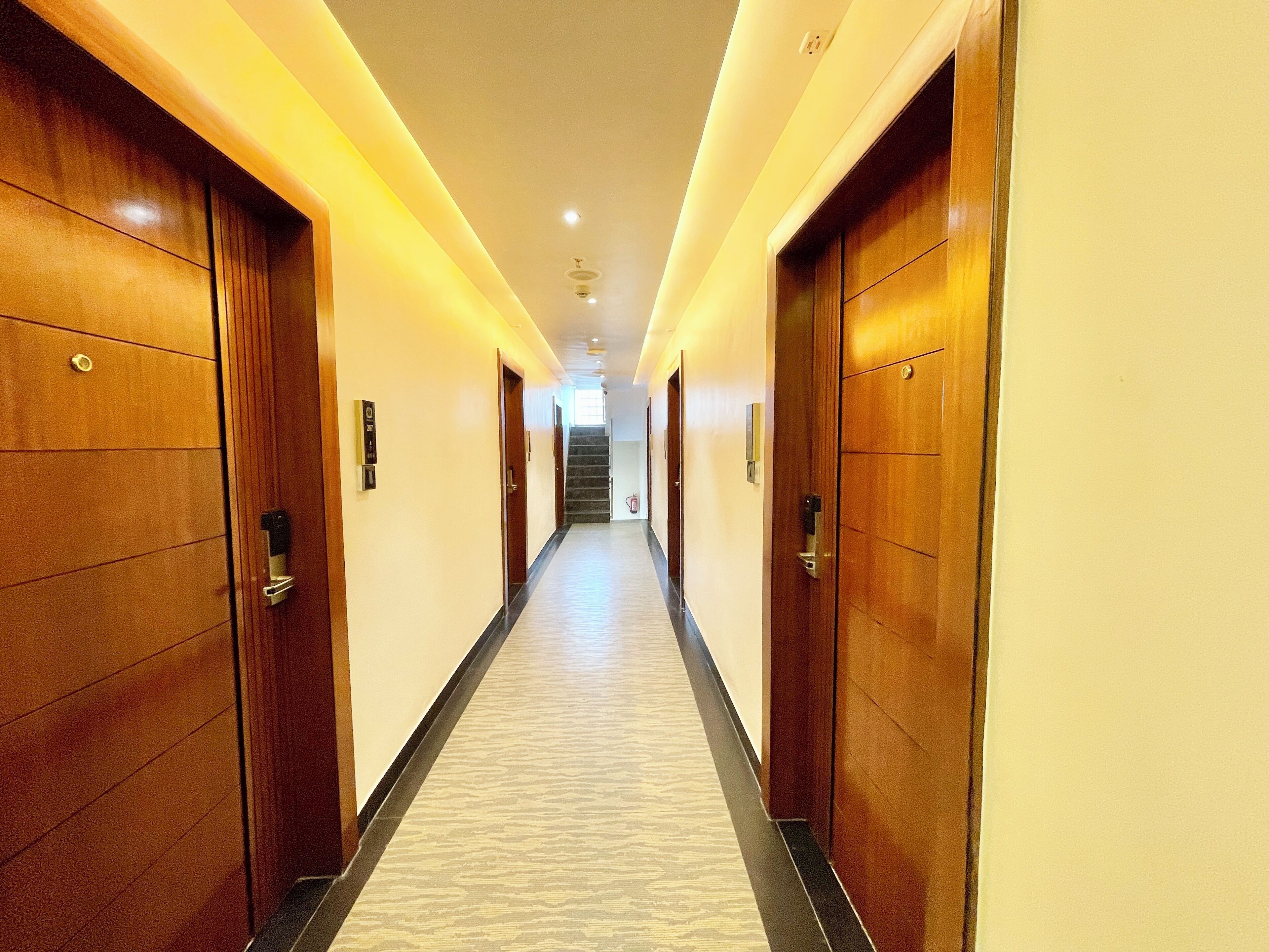 Un pasillo largo y estrecho con puertas de madera a ambos lados, que conduce a una escalera al final.