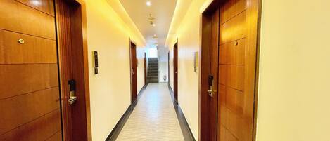 Un pasillo largo y estrecho con puertas de madera a ambos lados, que conduce a una escalera al final.
