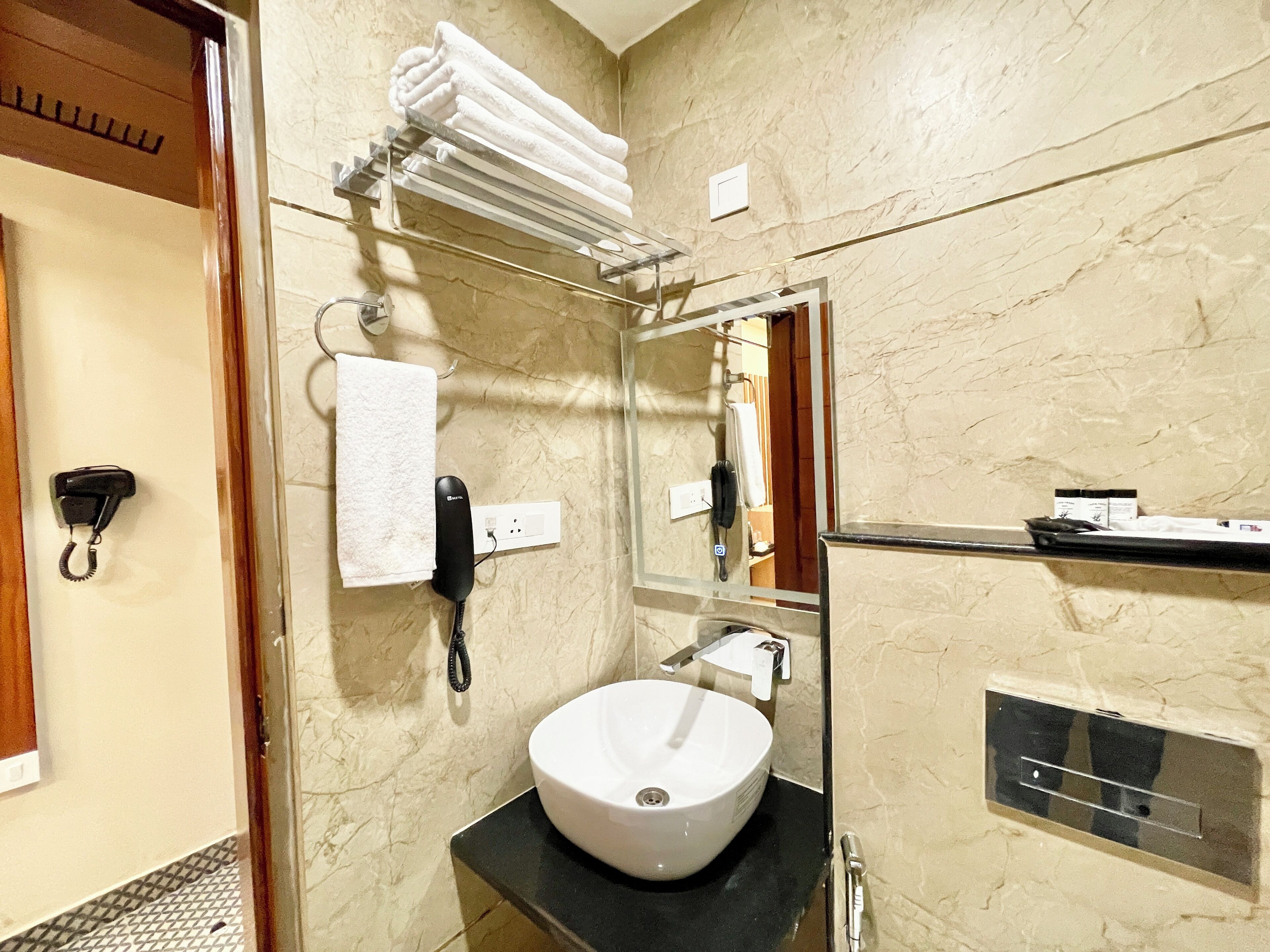 Une salle de bain avec un lavabo blanc, un porte-serviettes avec des serviettes pliées, un téléphone et un miroir.