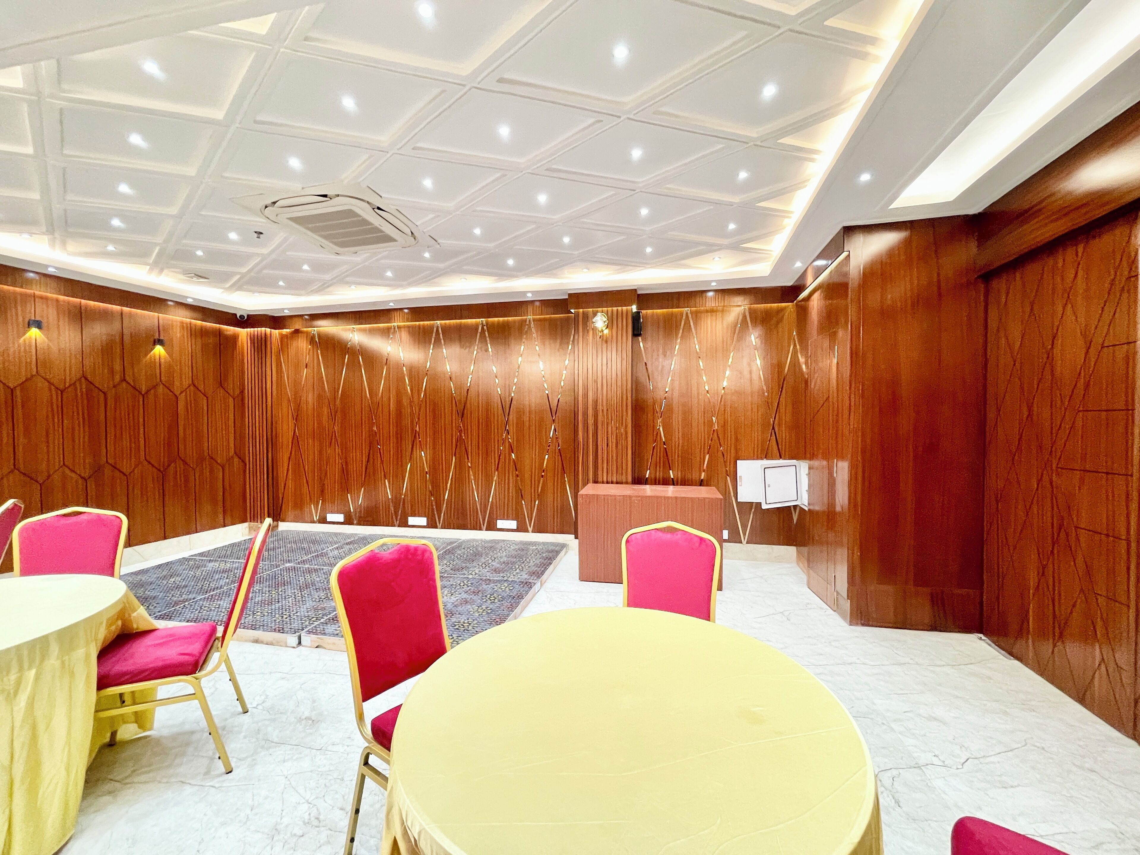 Ein Konferenzraum mit runden Tischen und Stühlen, einem Rednerpult und einer Wand mit Holzverkleidung.