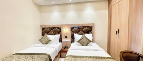 A hotel room with two beds, a wooden wardrobe, a bedside table with a lamp, and a chair.