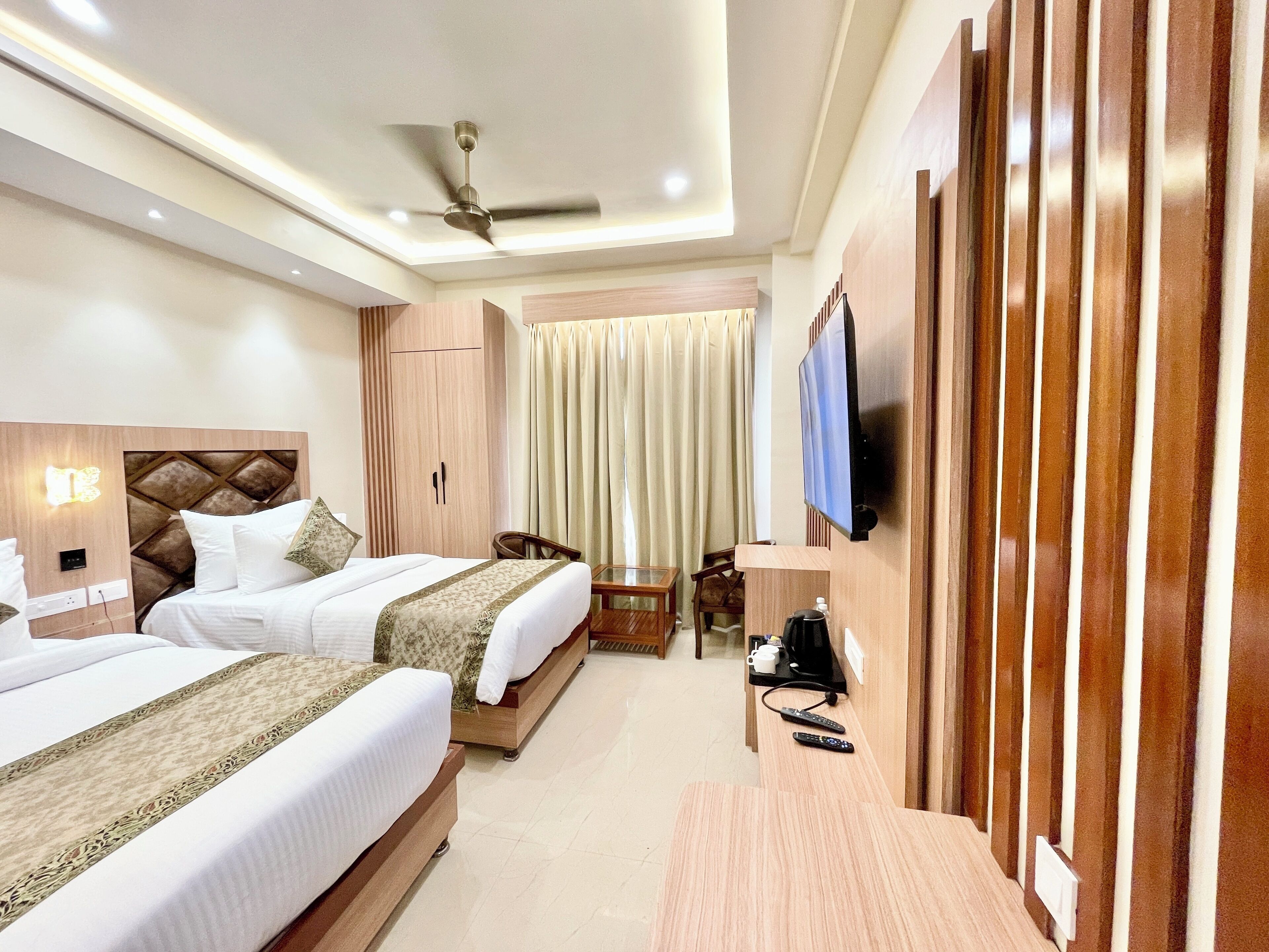 A hotel room with two beds, a ceiling fan, a TV mounted on the wall, a coffee maker, and a small table.