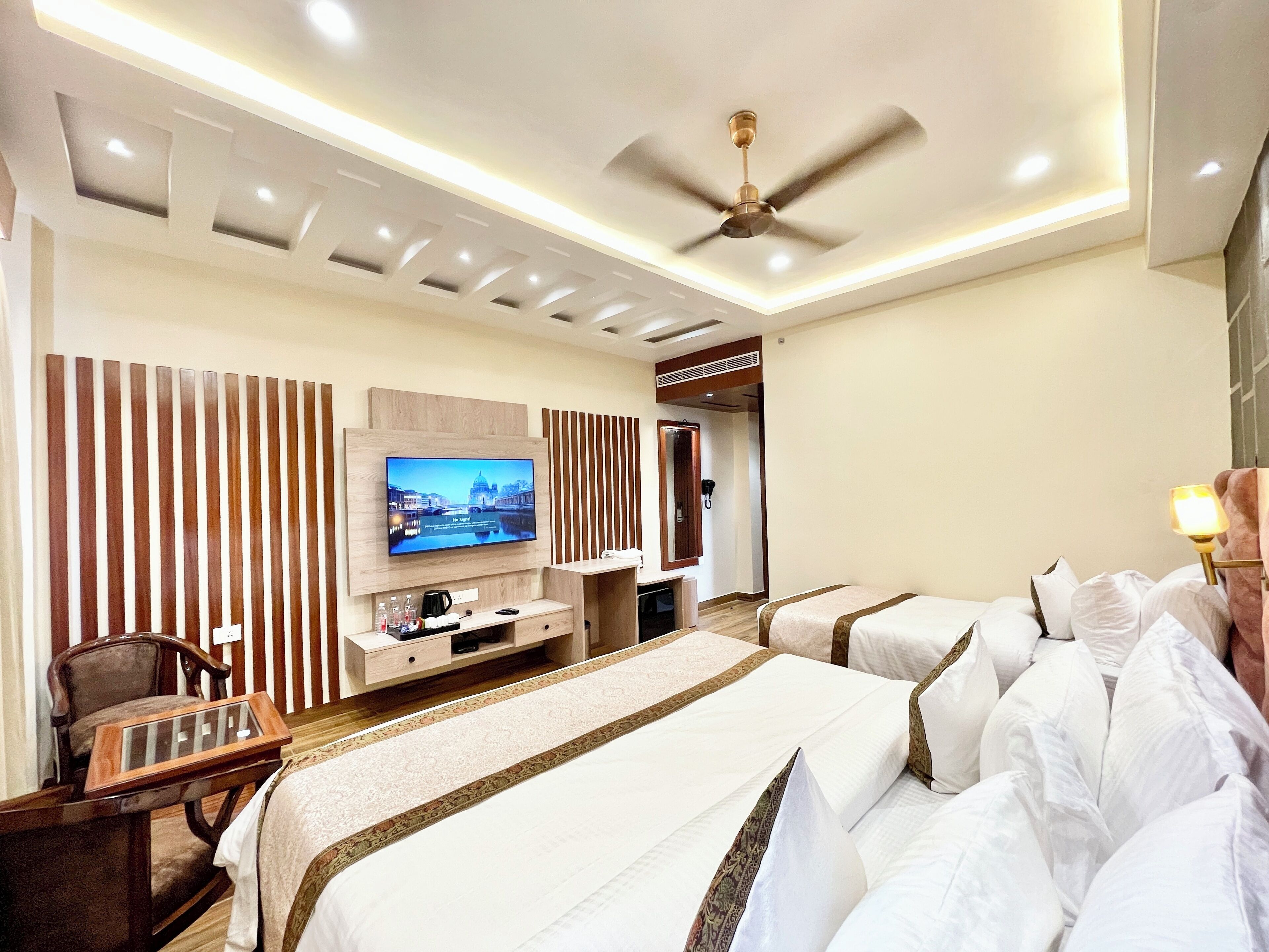 A hotel room with a large bed, a TV mounted on the wall, a ceiling fan, and a desk with a chair.
