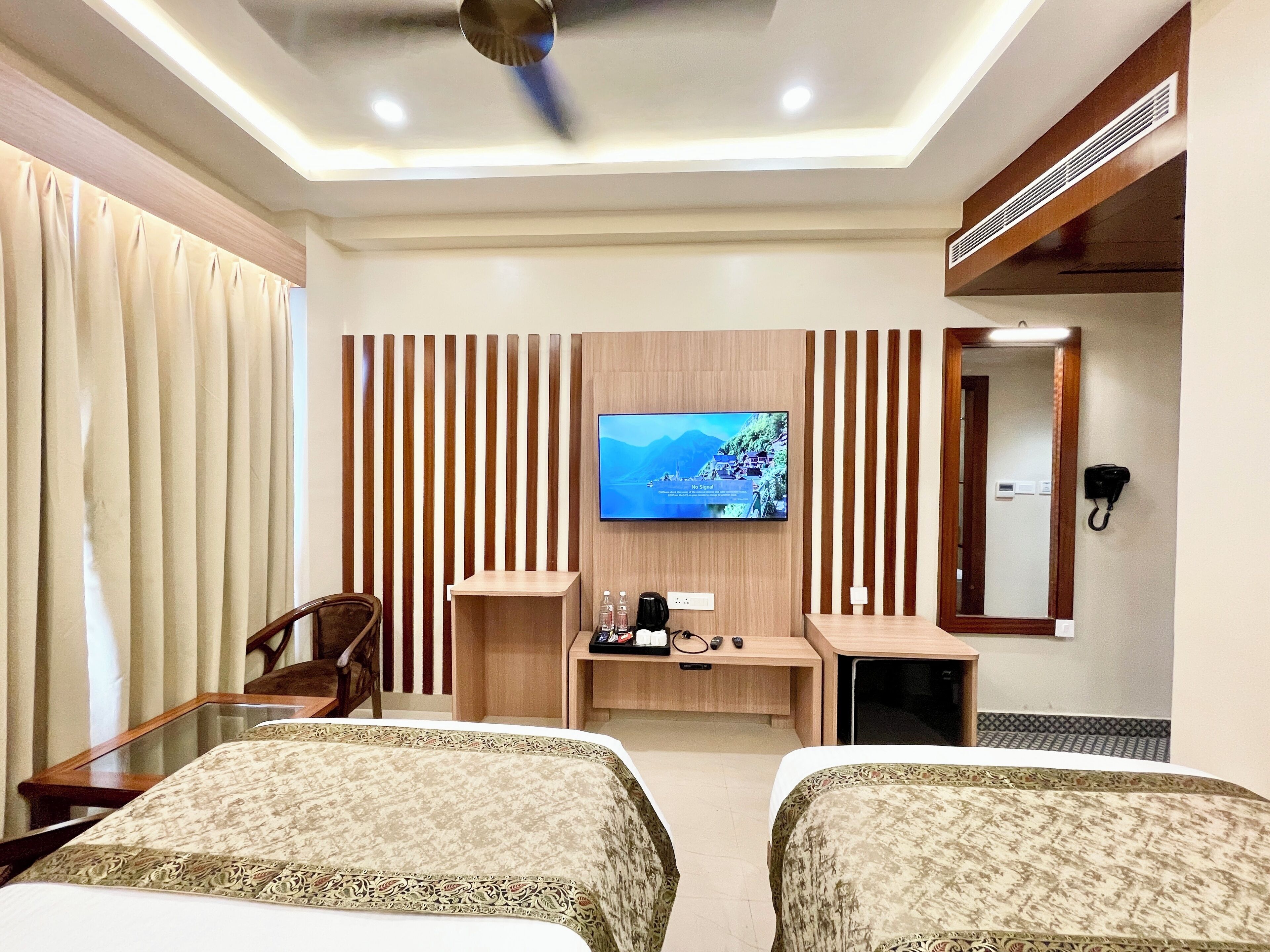 A hotel room with two beds, a TV, a desk, a chair, and a mirror.