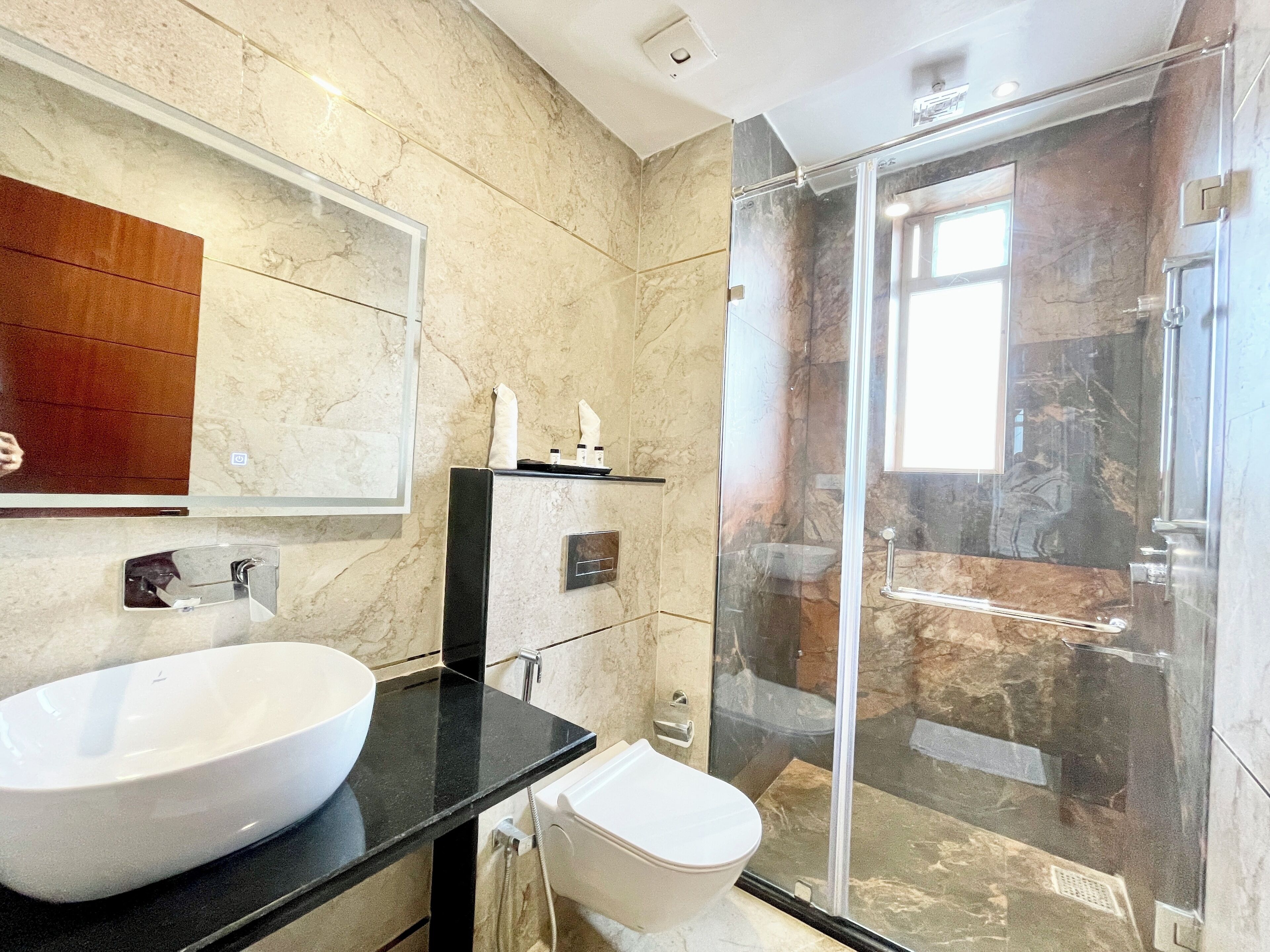 Un baño moderno con un lavamanos grande de color blanco, una cabina de ducha de vidrio y una pared revestida de mármol.