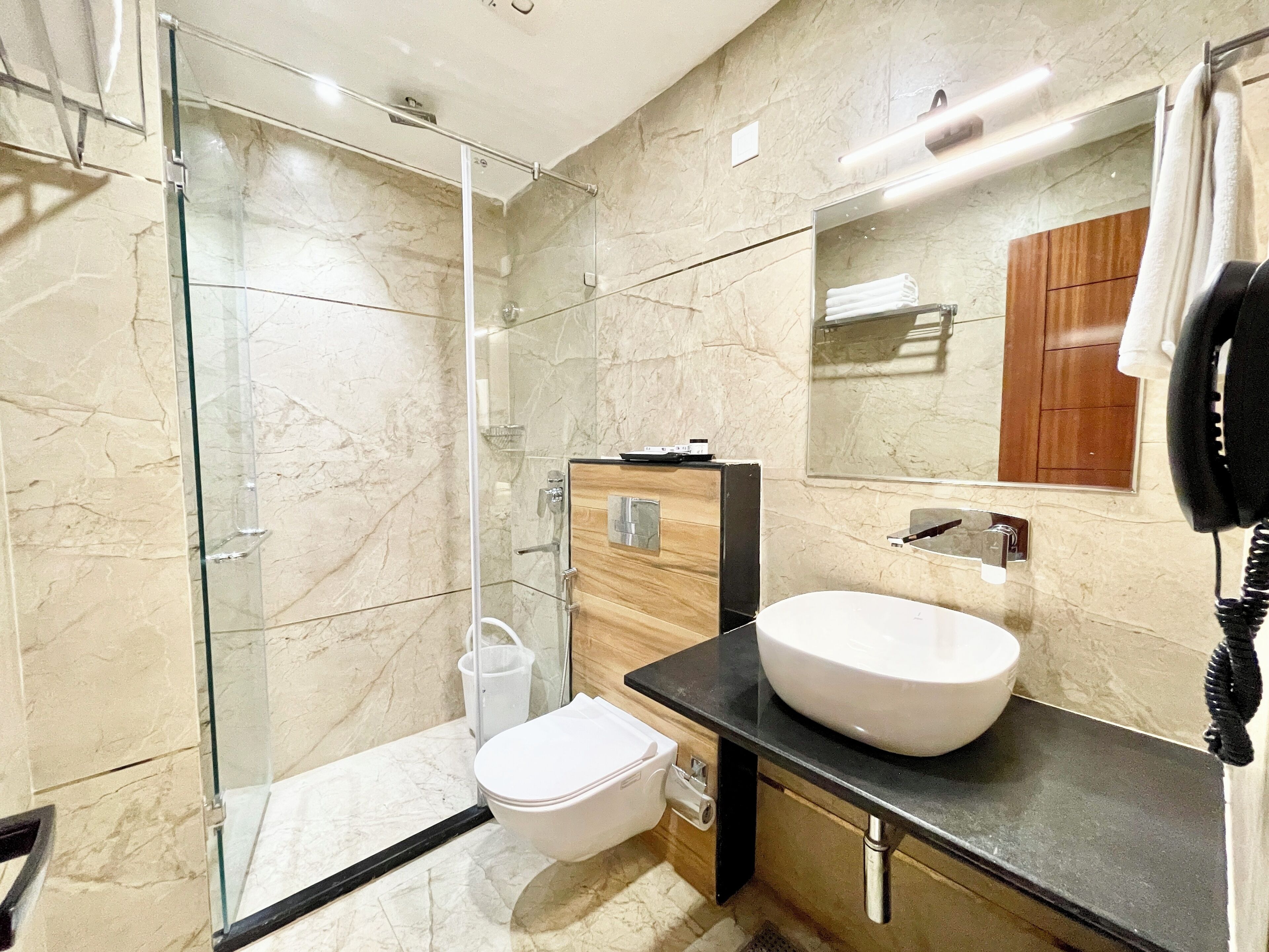 A modern bathroom with a glass shower enclosure, a white toilet, a wooden vanity with a large sink, and a mirror above the sink.