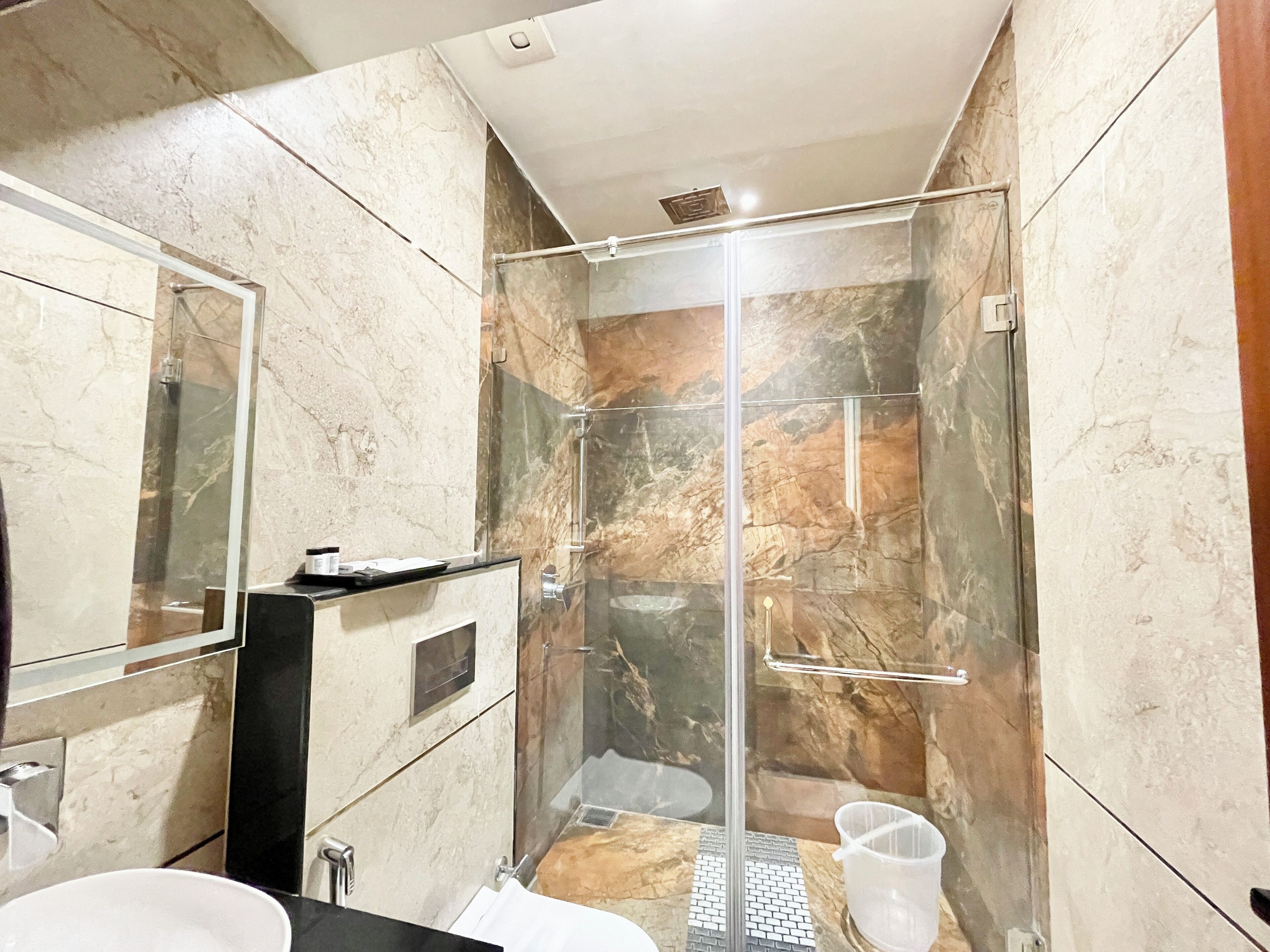 Un bagno moderno con cabina doccia in vetro, pareti in marmo e piano d'appoggio nero.