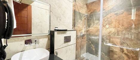 A modern bathroom with a marble wall, a glass shower enclosure, a black countertop, a white sink, and a white toilet.
