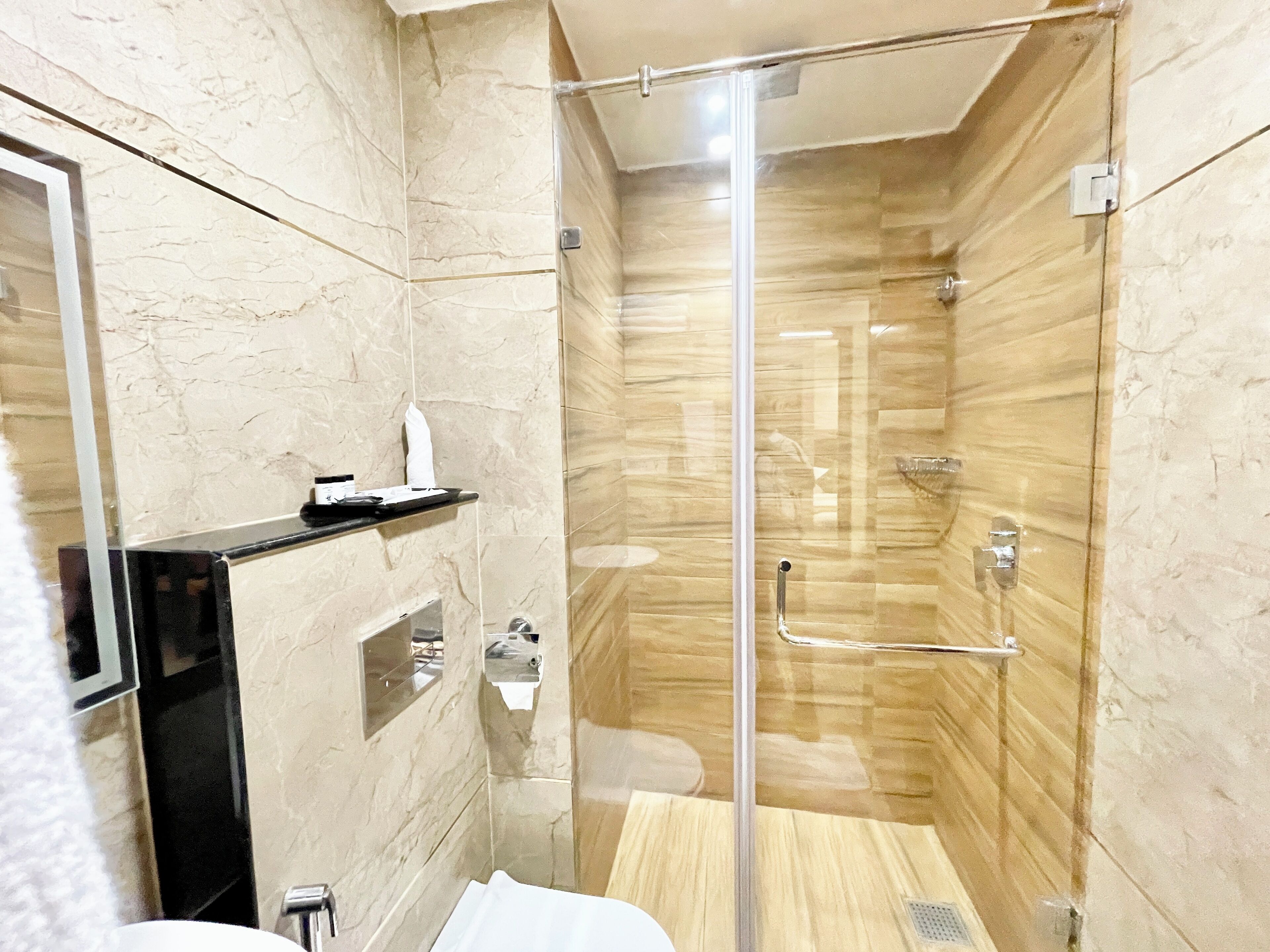 Un baño moderno con ducha envuelta en vidrio, paredes de mármol y tocador negro.