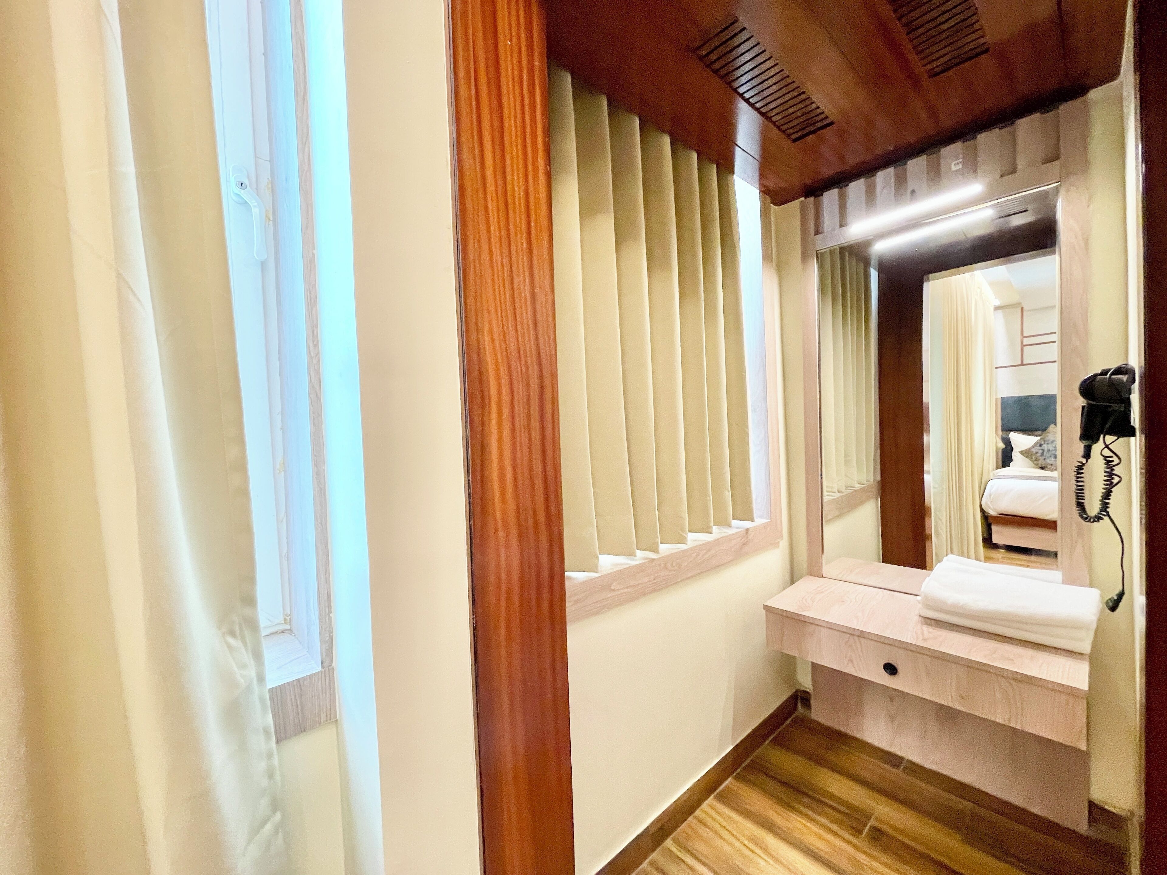 Een hotelkamer met een houten vloer, een kaptafel met spiegel, een bed met nachtkastje en een telefoon.