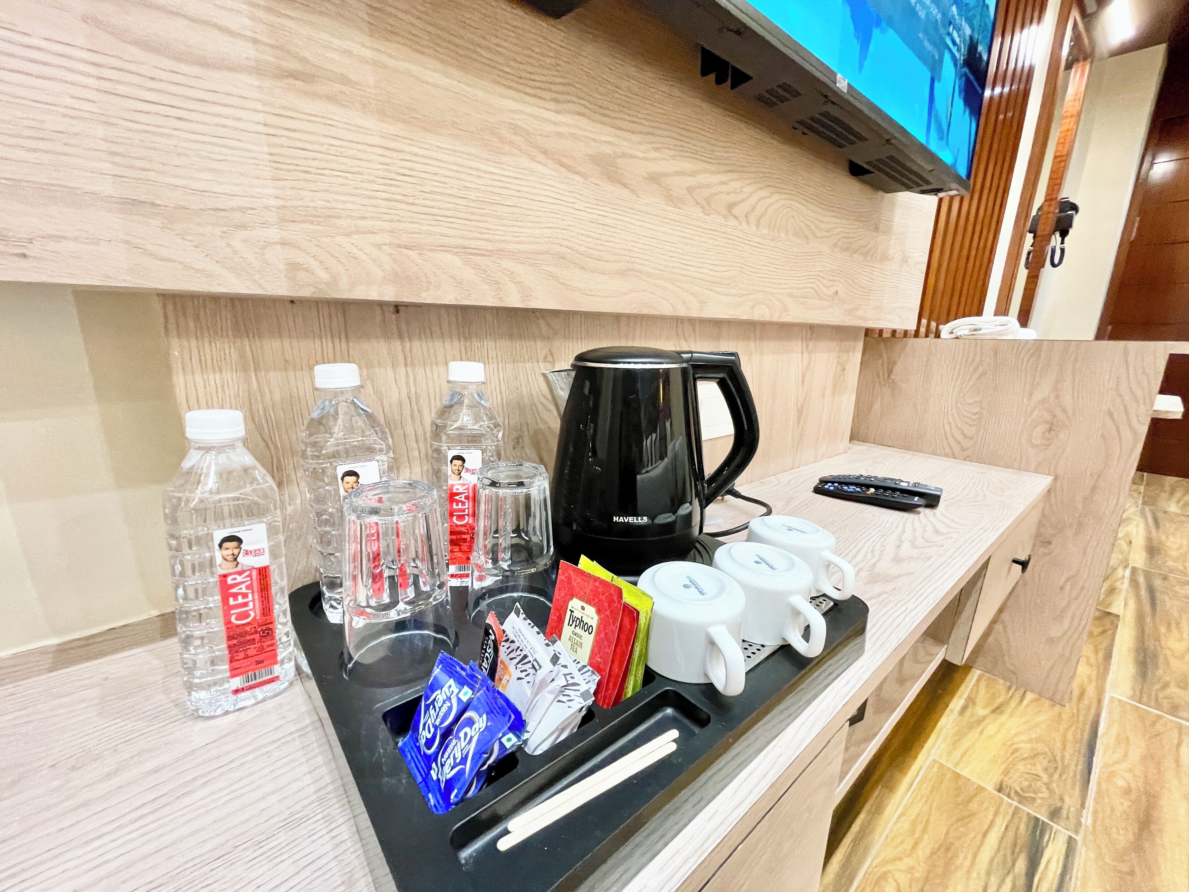 Cozinha compacta em quarto de hotel, com cafeteira, garrafas de água, sachês de chá e controle remoto.