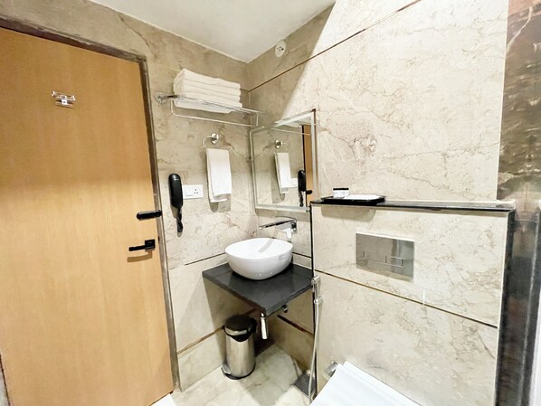 A modern bathroom with a marble wall, a sink, a mirror, a towel rack, and a trash bin.